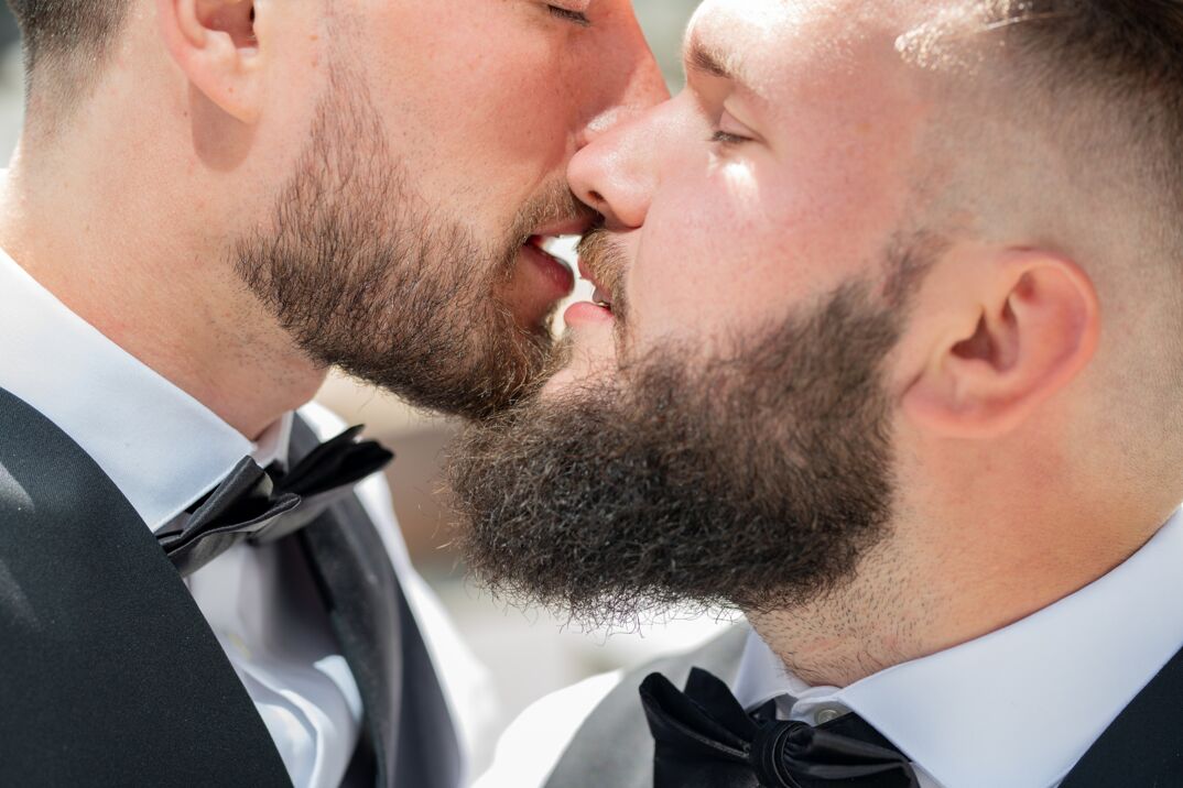 Two gay men in tuxedos kissing. 