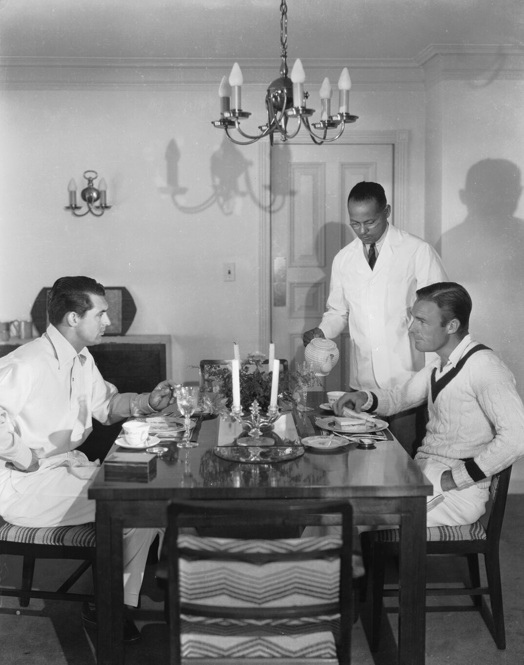 1935:  A servant pouring tea for the British born actor Cary Grant (1904 - 1986), born Archibald Leach, and the American actor, Randolph Scott (1898 - 1987) in the beach house which the two men shared during the 1930's, which was jokingly known as Bachelor Hall.  (Photo via John Kobal Foundation/Getty Images)