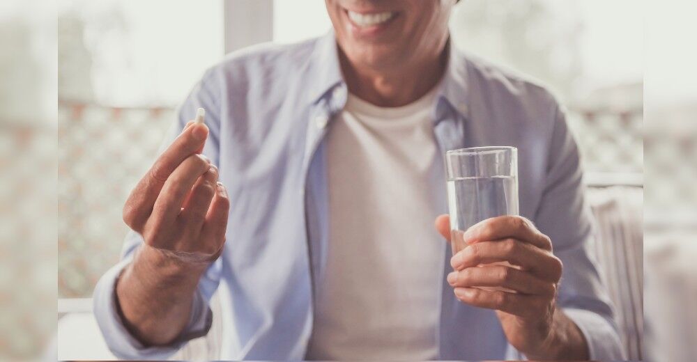 A man holds a glass of water and a pill