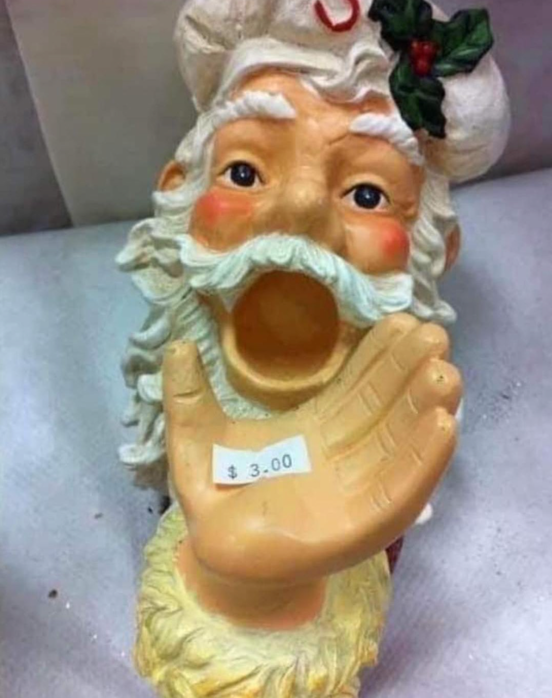 A ceramic Santa decoration, featuring Santa with a big white beard and hat looking up with his mouth wide open. His hand is outstretched in front of him with a price sticker that reads "$3.00."