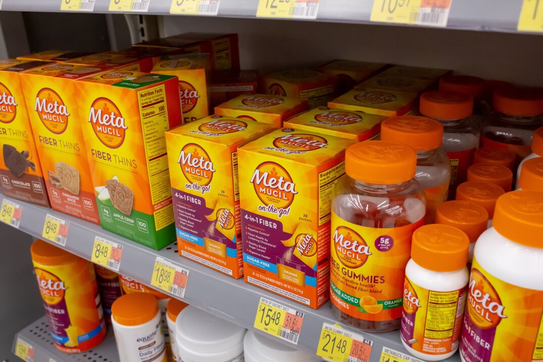A store shelf filled with orange boxed products and pill bottles all reading "Metamucil." Each label mentions something about fiber from "4 in 1 fiber" to "Fiber thins" and the shelf is well stocked.