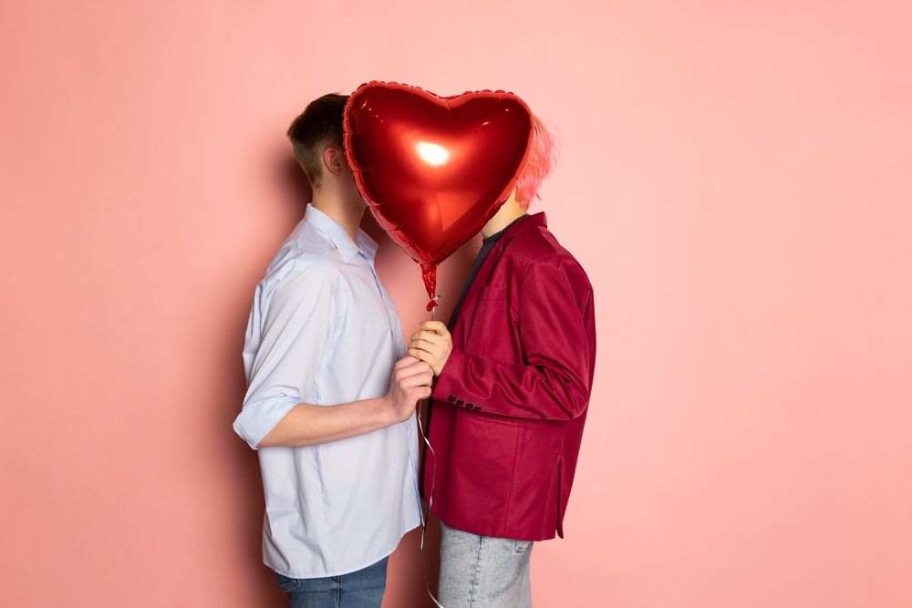 Two men kissing behind heart balloon