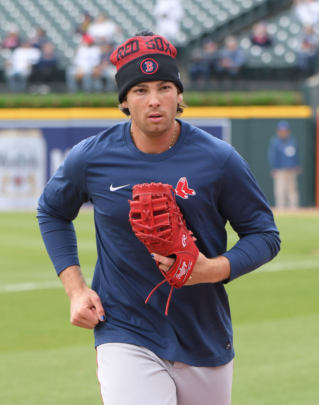 Triston Casas running on a baseball field wearing a Red Sox pullover and winter hat, with a red glove on his left hand. 