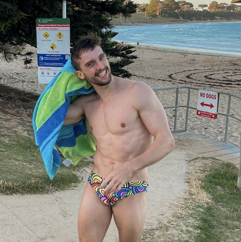 Heath Thorpe wearing a rainbow colored speedo on the beach.