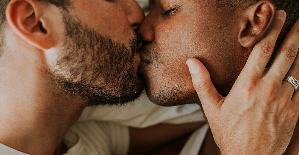 Two men kiss in bed