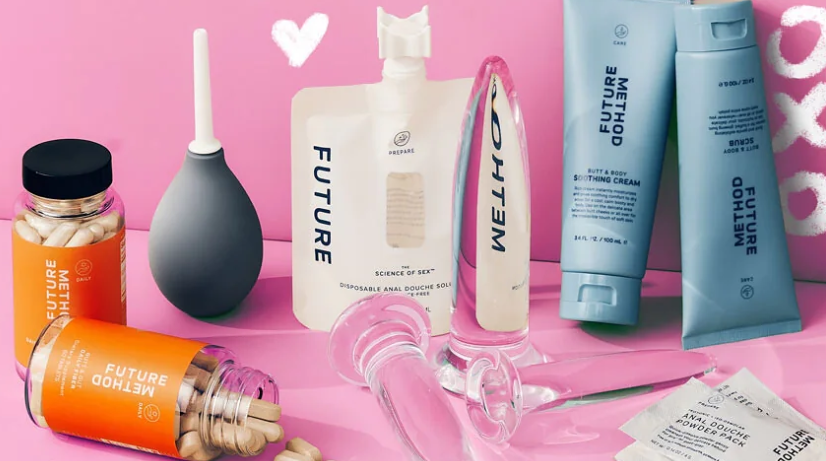 In front of a pink background, a handful of Future Method products are laid out, including a navy gray colored enema bulb, orange labelled pre and probiotics in clear medicine containers, glass anal toys, and blue squeeze bottles of soothing creams. All the products read "FUTURE METHOD" in capital letters.