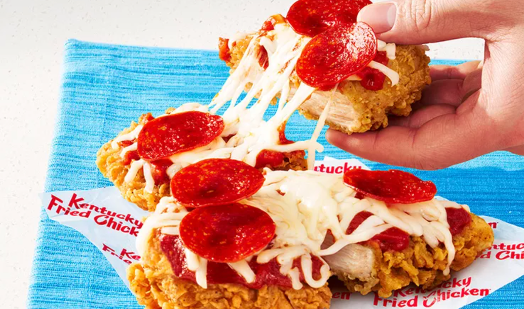 On a blue napkin rests two pieces of Kentucky Fried Chicken covered in mozzarella cheese, marinara sauce, and pepperoni in the fast food chain's new menu item: the Chizza. A hand pulls apart one of the pieces, showing how melted and chewy the cheese on top is. 