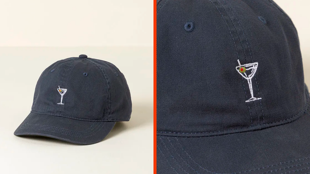 Two-panel image. On the left, a navy blue baseball hat with a line drawing of a martini with a green olive stitched in the center. In the right panel, a close-up of the white illustration. 