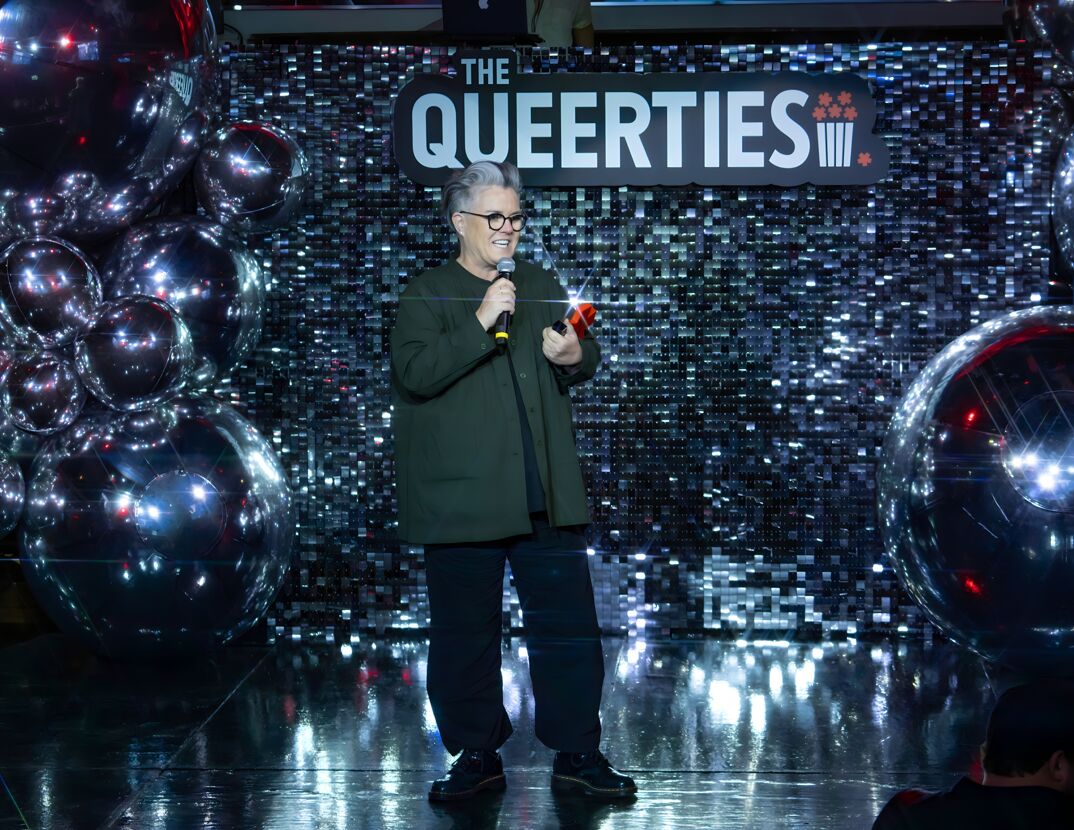 Rosie O'Donnell, in glasses with short gray hair, talks on stage at the 2024 Queerties Awards.