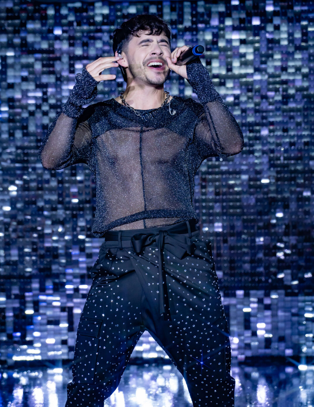 David Archuleta wears a black transparent long sleeved shirt and sparkling pants while performing on stage at the 2024 Queerties Awards.