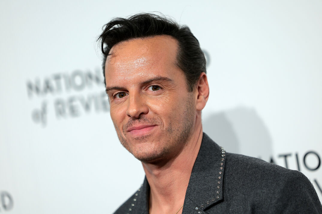 Andrew Scott smiles on the red carpet in a gray blazer with rhinestones along the collar. He has short brown hair coiffed up and light five o'clock shadow.
