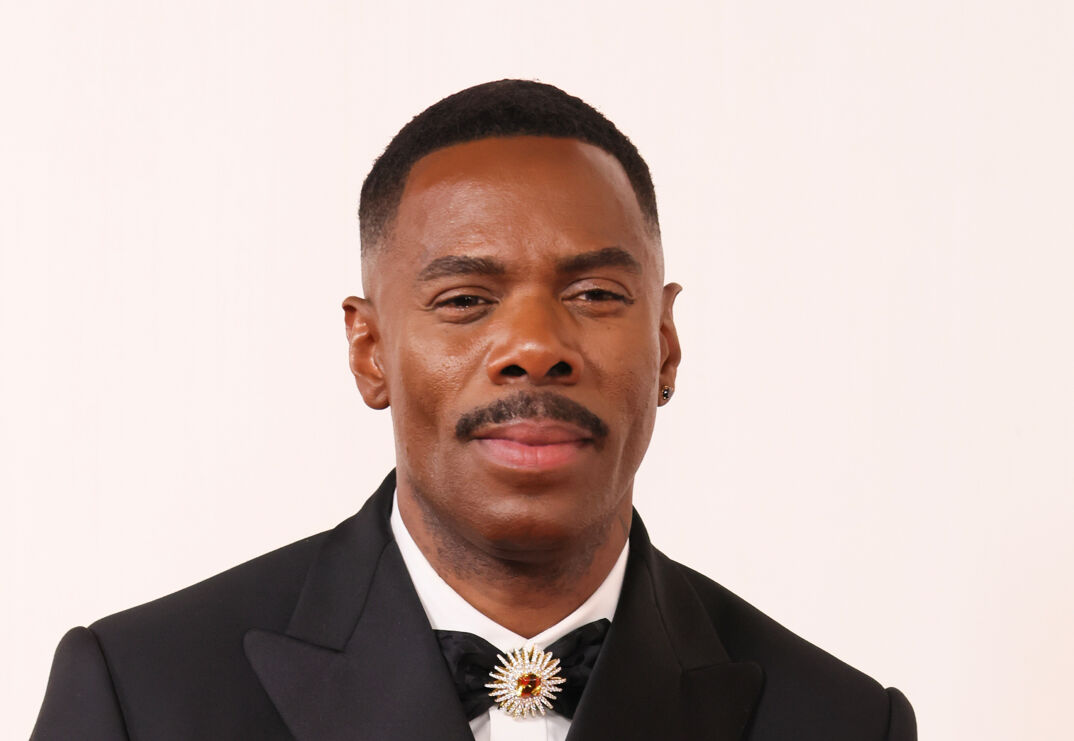 Colman Domingo, a Black man with short black hair and a thin black mustache, smiles on the red carpet. He wears a black tux and has a small earring in his left ear.