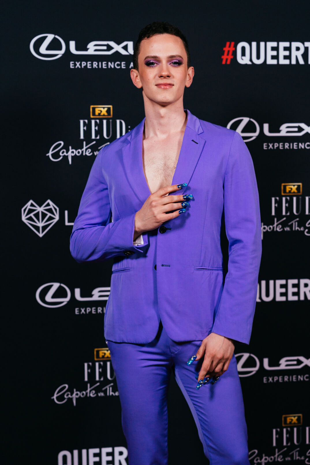 Matt Bernstein smiles in front of a black step-and-repeat in a light blue blazer at the 2024 Queerties Awards.