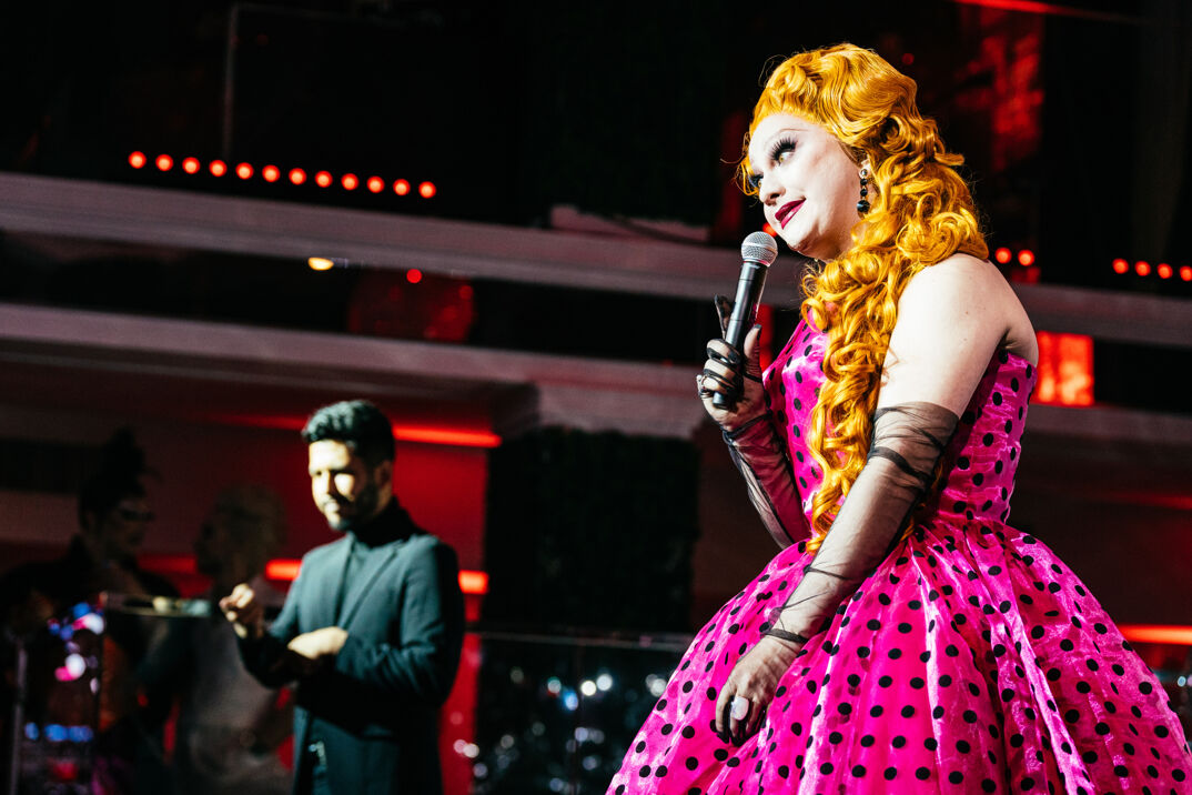 Jinkx Monsoon wears a pink dress in an orange long curled wig while presenting at the 2024 Queerties Awards.