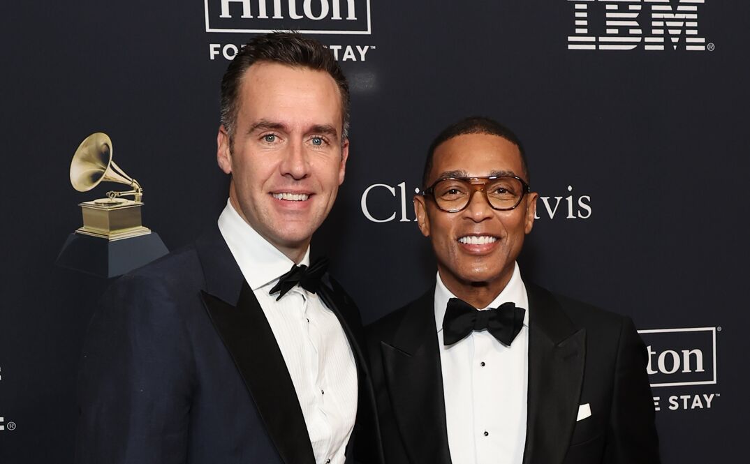 Tim Malone and Don Lemon smile on the red carpet in front of a black step-and-repeat at a Grammy party. Malone (left) wears a navy suit jacket over a white dress shirt, while Lemon (right) wears a black suit jacket. Both sport dark-colored bow-ties.