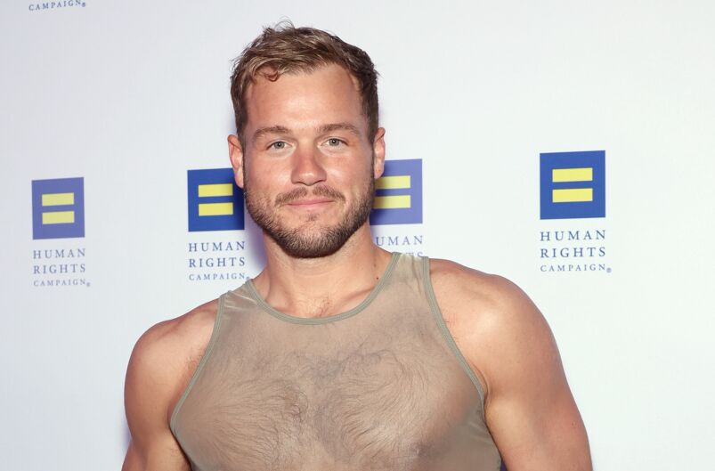 Colton Underwood smiles on the red carpet wearing a translucent tank top showing off his muscular and hairy chest.