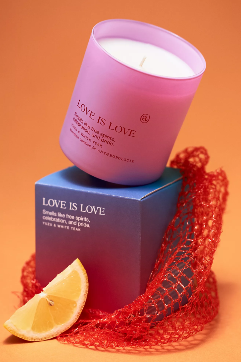 A pink glass candle pictured on top of a rainbow box that reads "Love is Love" and "Smells like free spirits, celebration, and pride."