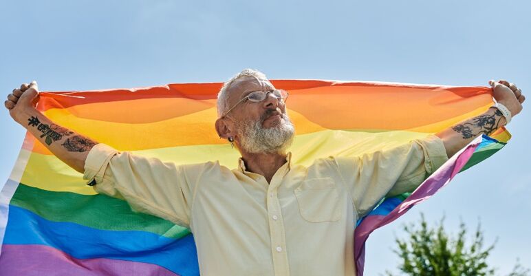 An older gay men carries a rainbow flag