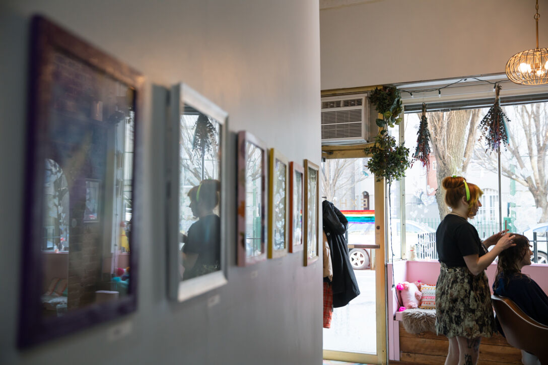 A row of framed photos on a wall with reflections of salon clients and stylists in the glass.