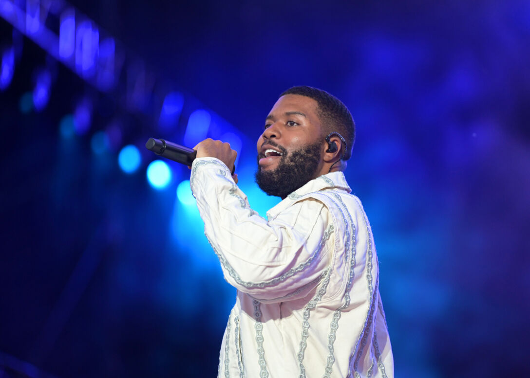 Khalid performs in a white button-down t-shirt in front of a blue screen.