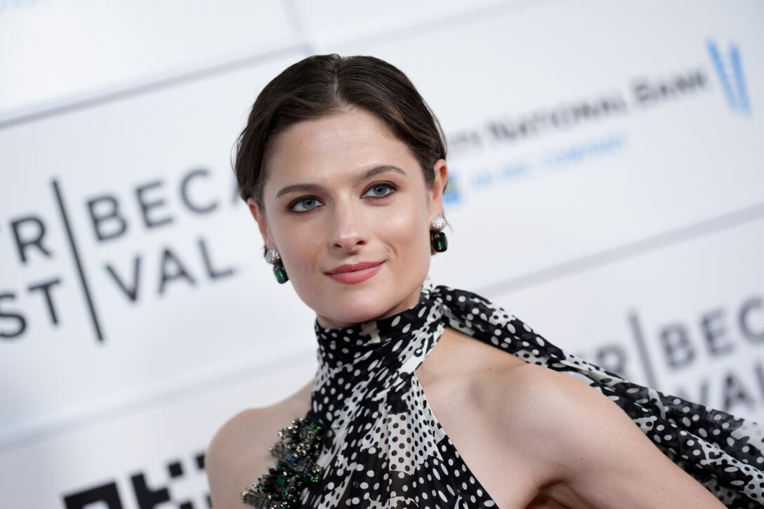 Louisa Jacobson poses in a black and white dress in front of a step-and-repeat on the red carpet.